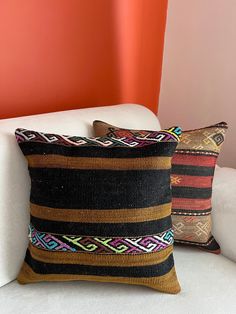 two pillows sitting on top of a white couch next to a red and orange wall