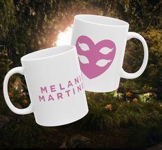 two white coffee mugs with pink masks on them