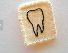 a tooth embroidered onto the side of a white piece of cloth with black thread on it