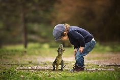 a young boy is playing with a small lizard in the grass while wearing a hat