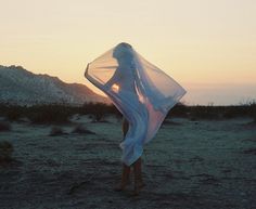 a woman standing in the middle of a desert holding a sheer fabric over her body