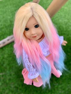 a doll with blonde hair and blue eyes is sitting on the grass, looking down