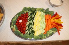 a platter filled with veggies and other vegetables on a table next to bowls of dips