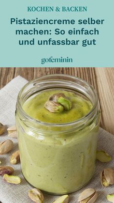 a jar filled with green smoothie sitting on top of a table next to nuts