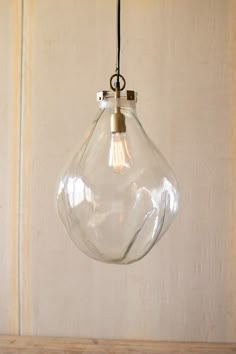 a clear glass light hanging from a metal hook on a wooden table with a white wall in the background