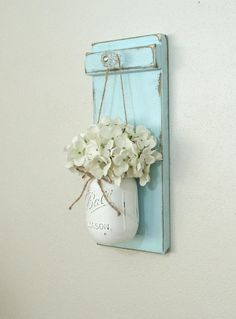 a mason jar filled with white flowers hanging from a blue painted frame on the wall