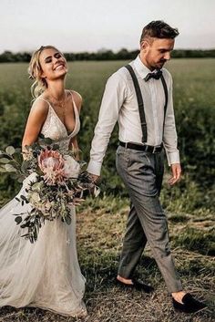 a bride and groom walking through a field