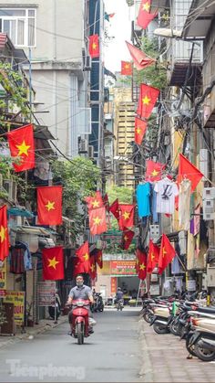 a man riding a motorcycle down a street filled with red and yellow flags hanging from buildings