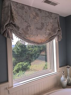 a bath tub sitting under a window next to a white vase with flowers on it