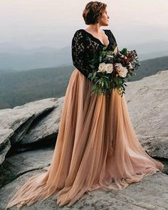 a woman standing on top of a mountain with a bouquet in her hand and looking at the sky