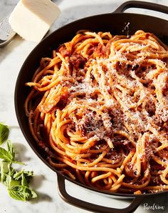 a skillet filled with pasta and sauce on top of a white counter next to parmesan cheese