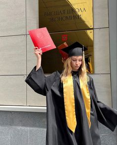 a woman in graduation gown holding up a red book