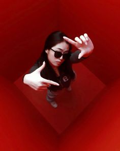 a woman wearing sunglasses making the vulcan sign with her hand while standing in a red room