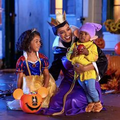 a woman and two children dressed up as disney characters with pumpkins on the ground