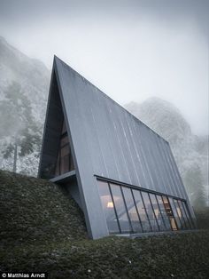 an unusual house on the side of a hill with mountains in the background and foggy sky