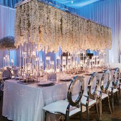 a long table is set up with white flowers and silver chairs for an elegant wedding reception