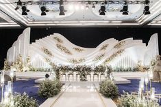 a stage set up for an event with flowers and greenery on the floor, surrounded by white chairs