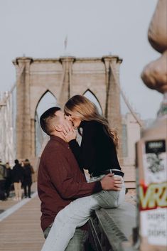 a man and woman kissing in front of the brooklyn bridge