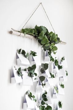 a white wall hanging with green plants and notes attached to the side, on a string