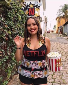 a woman standing in front of a wall holding a popcorn bucket and wearing a necklace