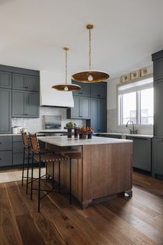 a kitchen with wooden floors and gray cabinets, two pendant lights above the island counter