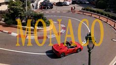 a red car driving down a street next to a parking lot with cars parked on it