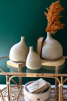 three white vases sitting on top of a glass table next to a brown plant