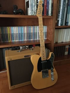 an electric guitar and amp sit on the floor in front of a bookshelf