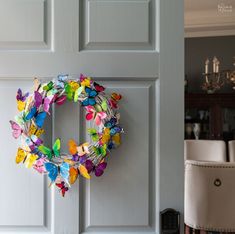 a colorful wreath hanging on the front door of a house with white chairs and chandelier in the background