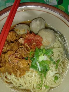 a bowl filled with noodles, meat and veggies next to chopsticks