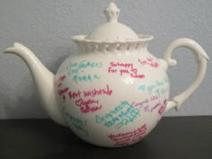 a white teapot with writing on it sitting on top of a black table next to a wall