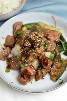 a white plate topped with meat and veggies next to a bowl of rice