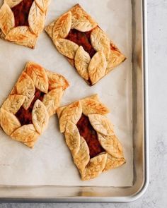 four pieces of pie sitting on top of a baking pan covered in sauce and leaves