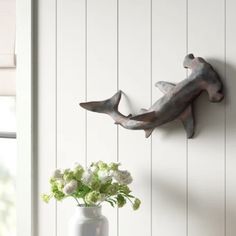 a vase with flowers in it sitting next to a metal dolphin wall decoration on the wall