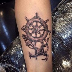 a black and white tattoo on the leg of a person with an anchor, steering wheel and anchors