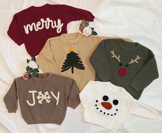 four sweaters with christmas designs on them sitting on a white sheet in the shape of a snowman