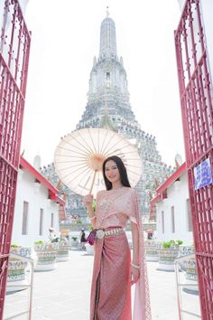 a woman standing in front of a building holding an umbrella and wearing a pink dress