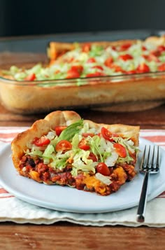 a slice of vegetable pizza on a plate with a fork and serving dish in the background