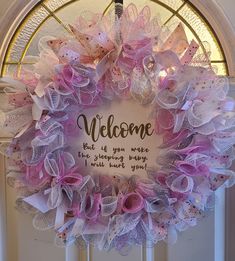 a welcome wreath with pink and white bows hanging on the front door to someone's house