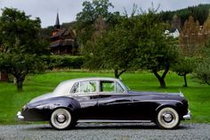 an old black car is parked on the gravel