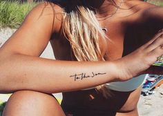 a woman is sitting on the beach with her arm tattoo that says to the sun