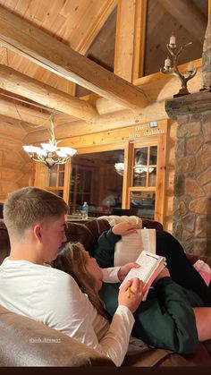 a young man and woman sitting on a couch reading books in front of a fireplace