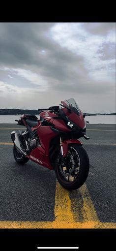 a red motorcycle parked on the side of a road next to a body of water