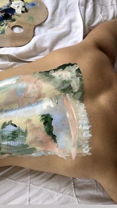 a person with paint on their stomach laying down next to a painting palette and brush