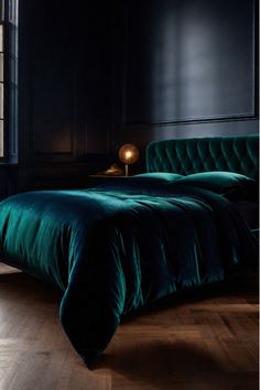 a green velvet bed in a dark room with wooden flooring and black headboard