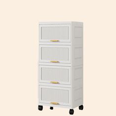 a white cabinet with four drawers on wheels and gold handles, against a beige background