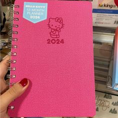 a person holding a pink notebook with a hello kitty sticker on the front cover