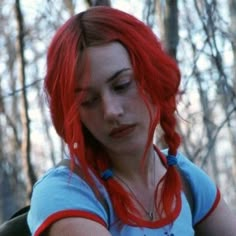 a woman with red hair and blue shirt looking at her cell phone in the woods