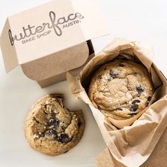 a cookie in a paper bag next to a box with a chocolate chip cookie inside