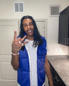 a man in a blue vest making the peace sign with his hand while standing next to a kitchen counter